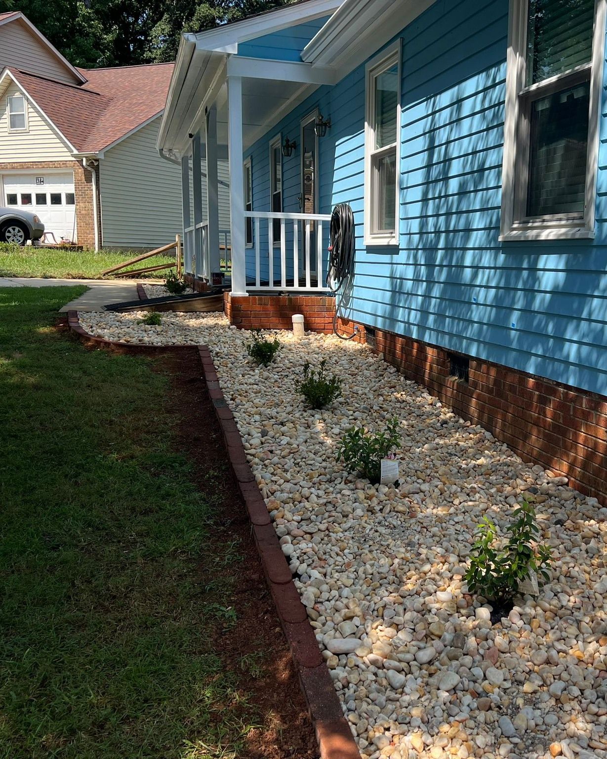 A blue house with a white porch and gravel in front of it