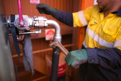 Worker in yellow and blue work clothes using a wrench on pipes and valves.