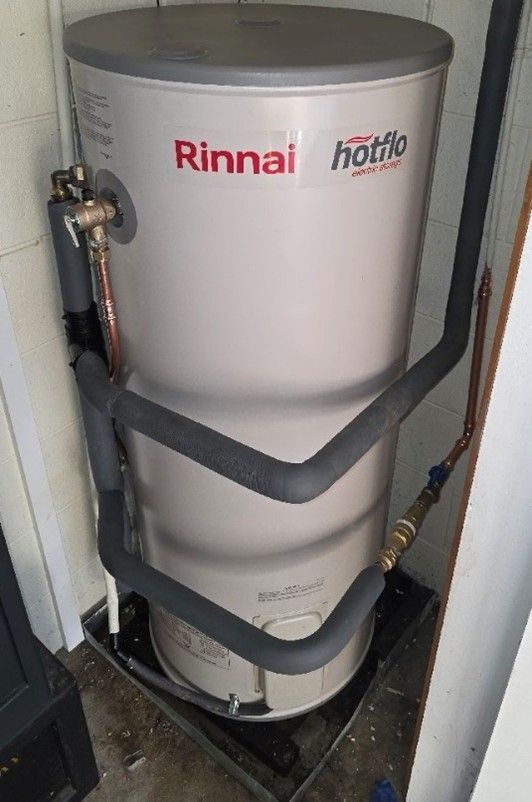 Rinnai Hotflo water heater. Cylindrical, silver tank with insulated pipes in a corner.