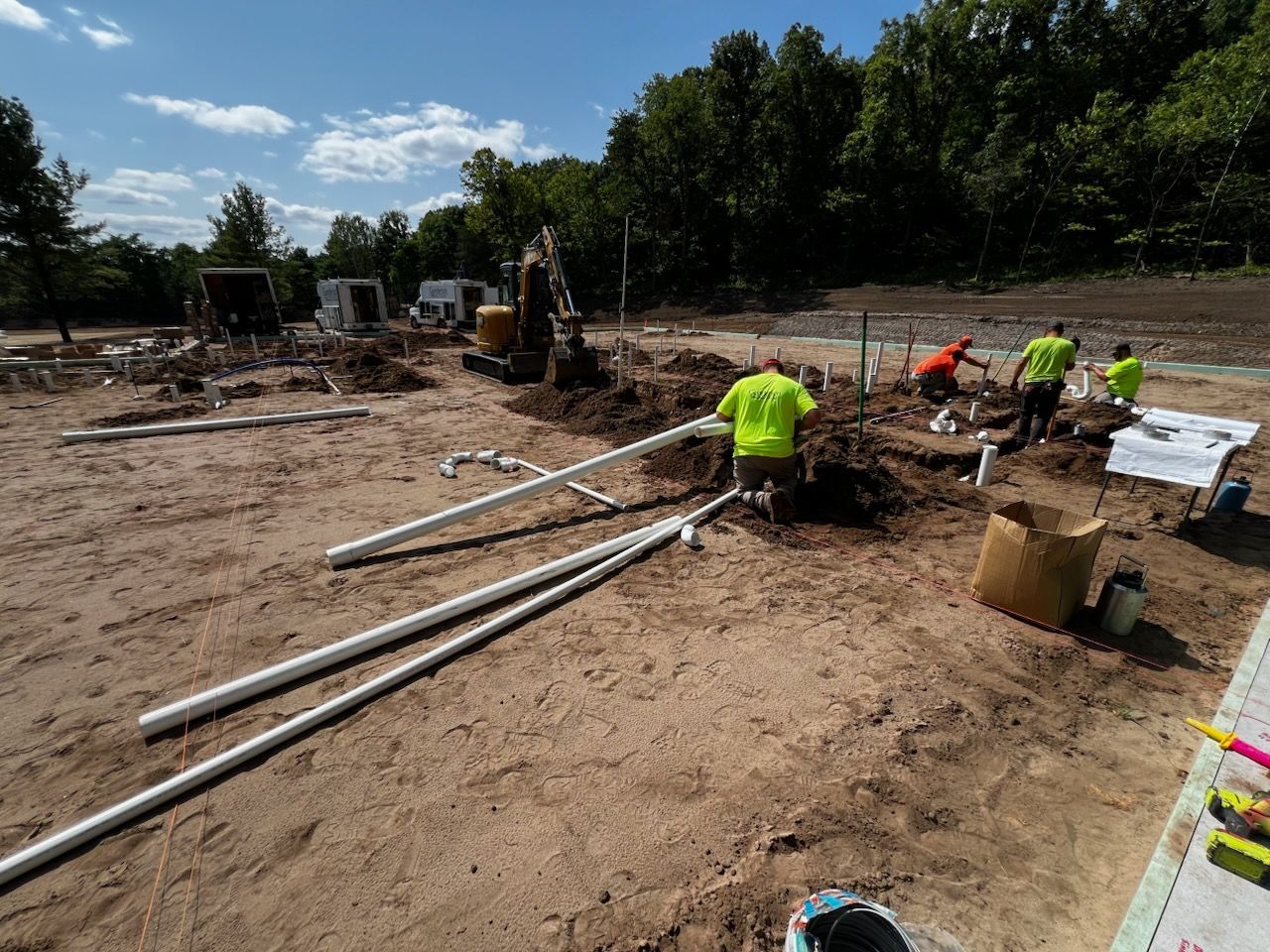 Construction site with workers in neon green shirts installing white pipes outdoors.