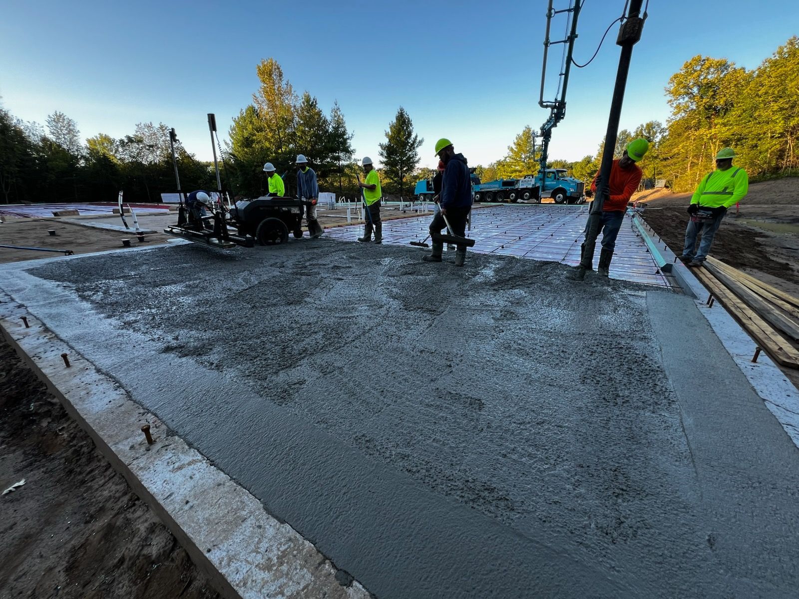 Construction workers pouring concrete foundation; a concrete pump is used on site.