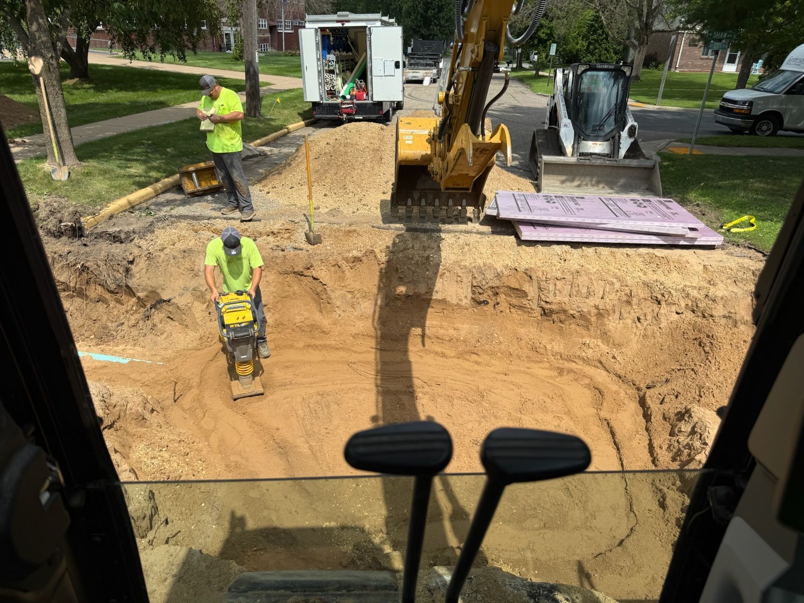 Construction site: Workers operate heavy machinery, including an excavator, compacting soil in an open pit.