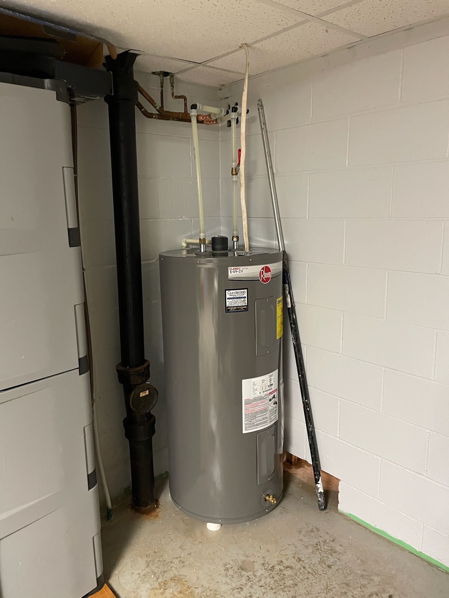 Water heater in a basement corner with pipes and a black flue.