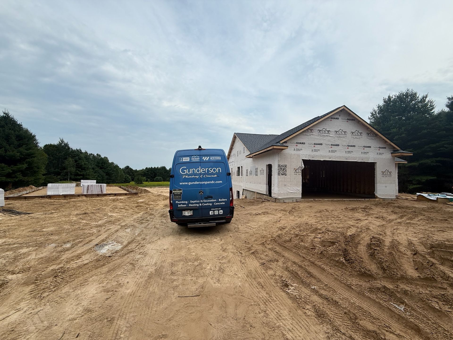 A blue van parked in front of a house under construction on a muddy dirt lot.