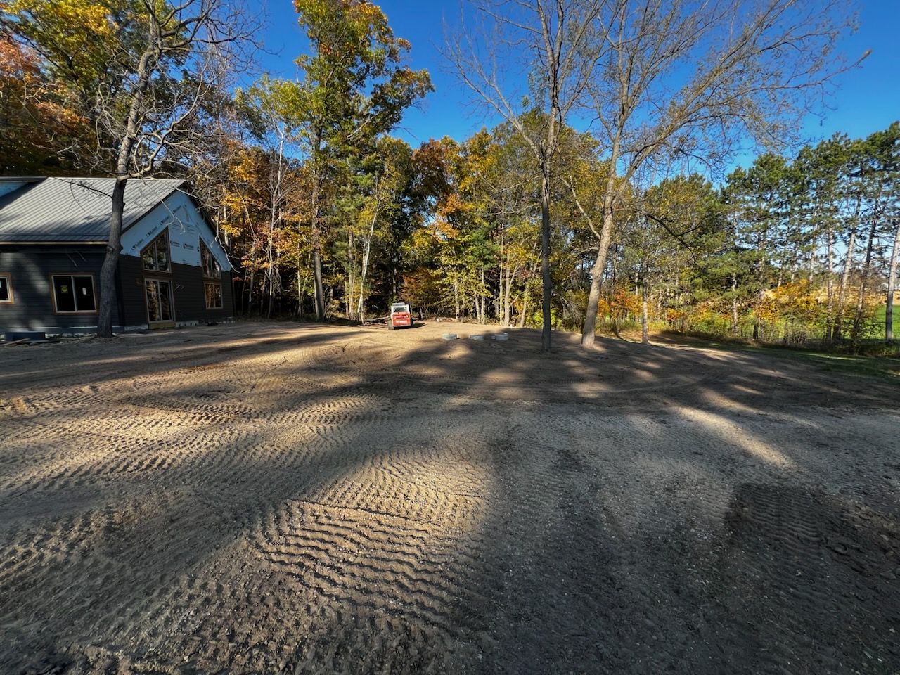 A construction site with a building under construction, surrounded by trees with autumn leaves.