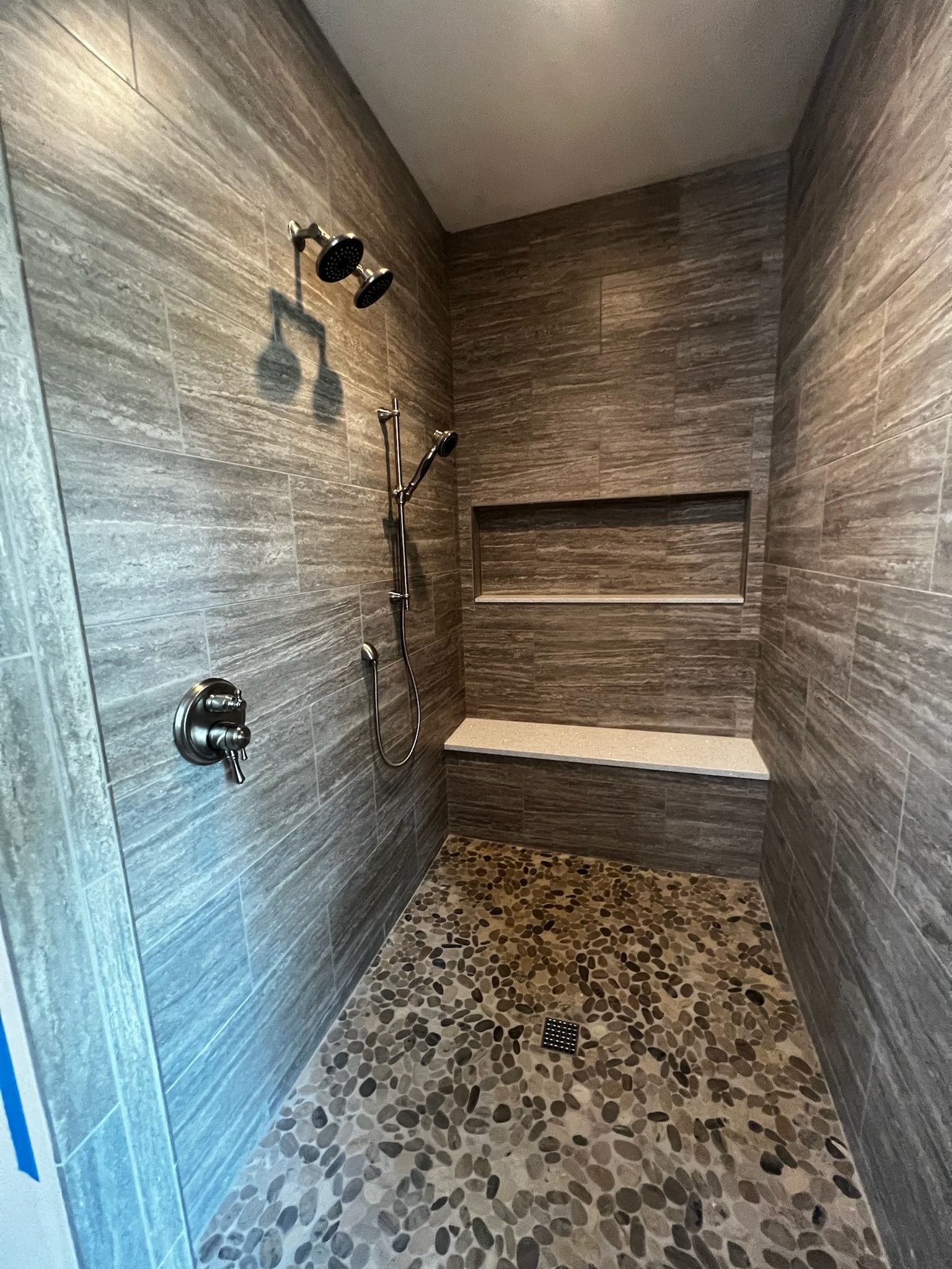 Gray tiled shower with pebble floor, bench, and dual shower heads.