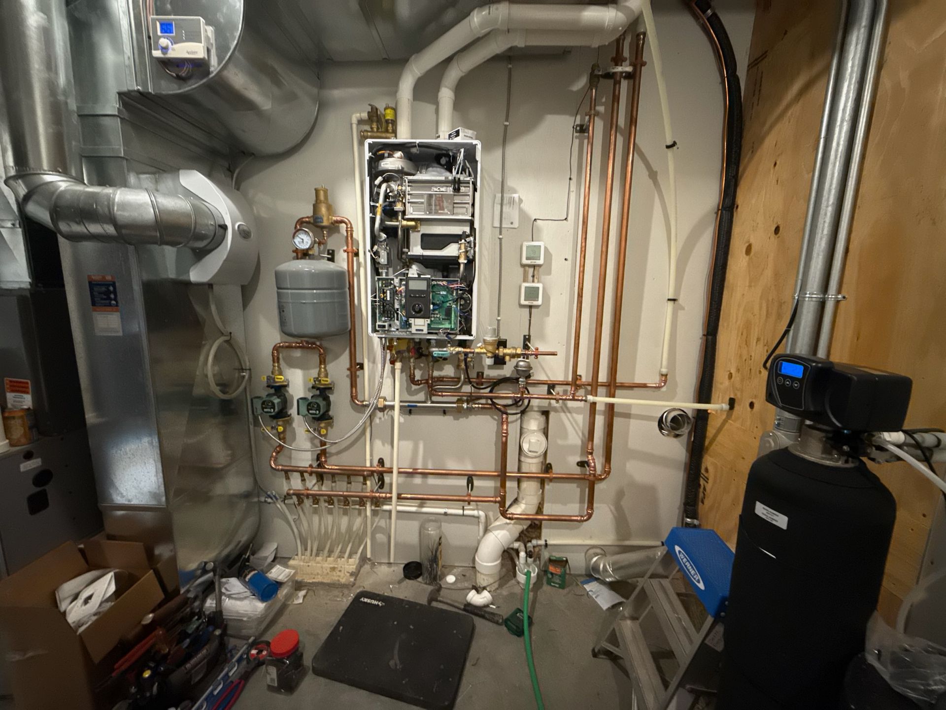 A boiler and water heater installation in a utility room with copper pipes, water softener and other equipment.