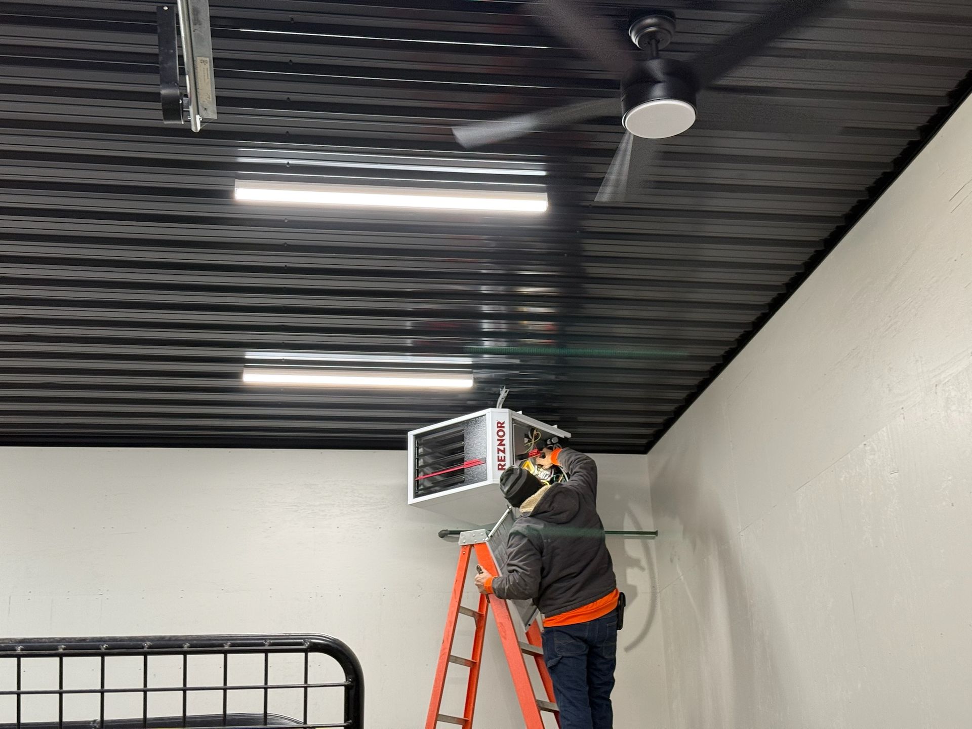 Person on a ladder installing equipment on a black textured ceiling in a room with white walls.