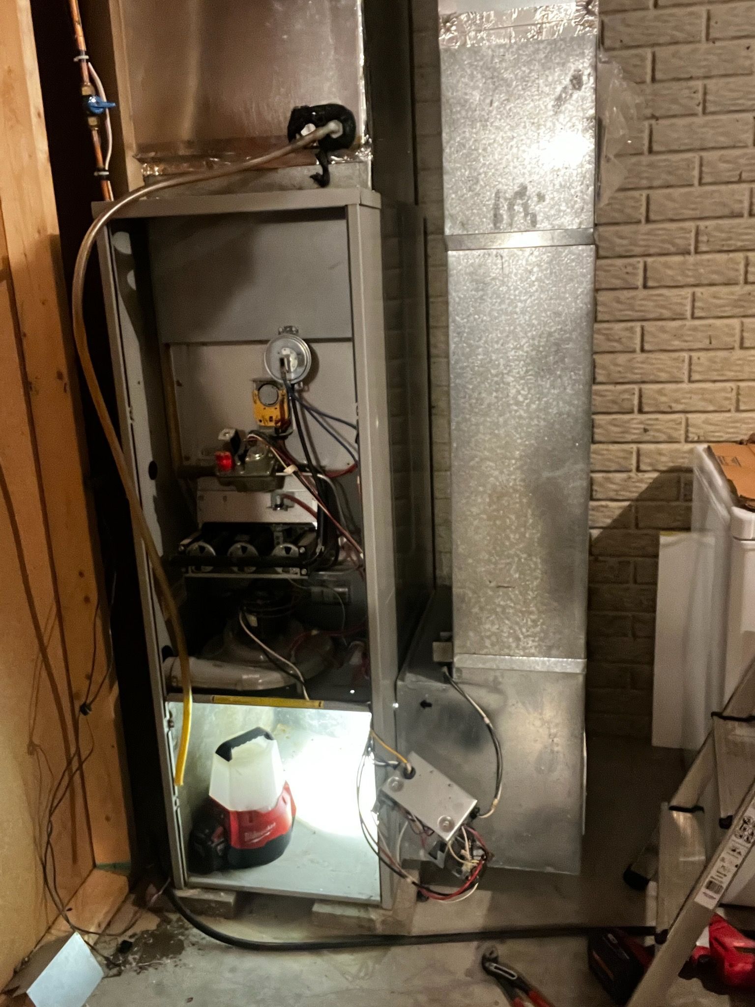 Furnace with open access panel, metal ductwork, and interior components in basement.