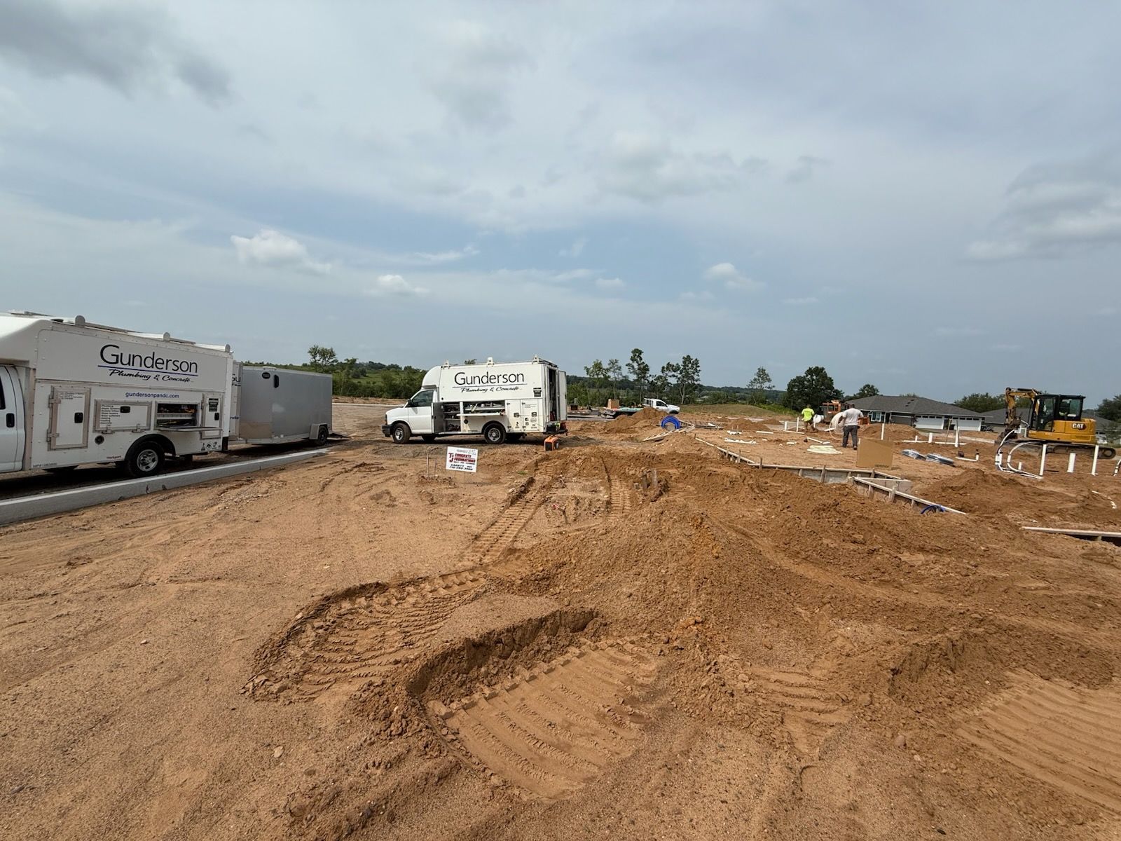 Construction site with dirt, equipment, and white service trucks under a cloudy sky.