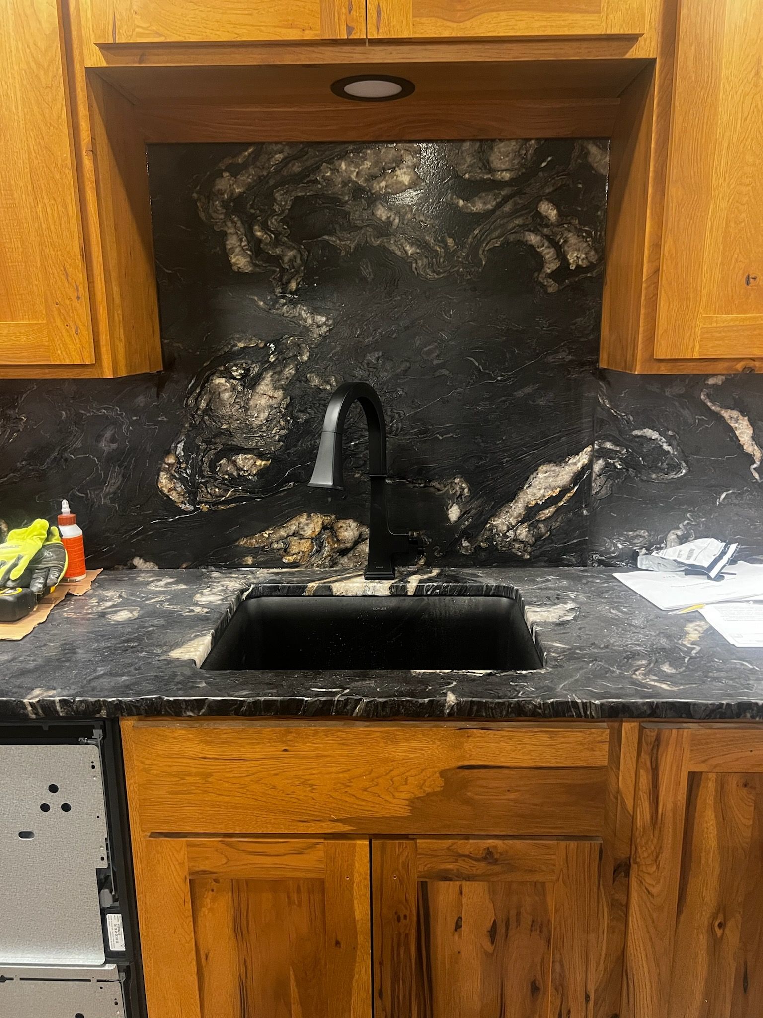 Black granite kitchen sink with a black faucet, surrounded by wooden cabinets.