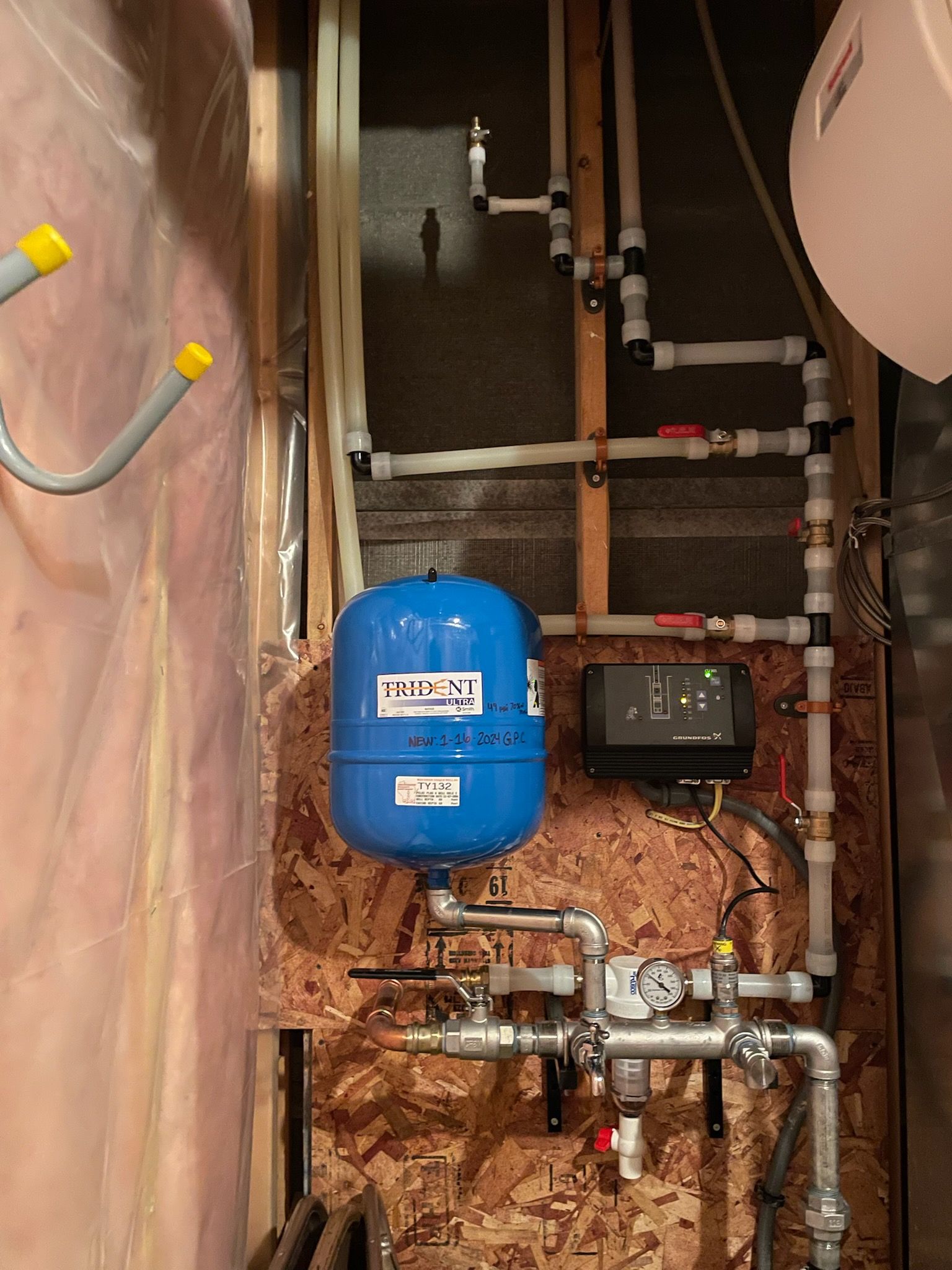 Plumbing system with blue expansion tank, pipes, and control panel in a basement.