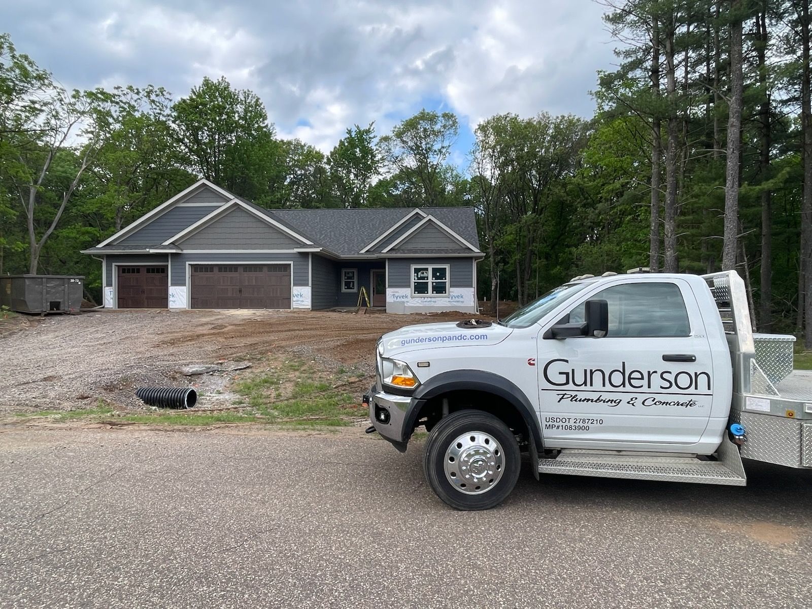 A white plumbing truck in front of a newly constructed house with gray and brown exterior.