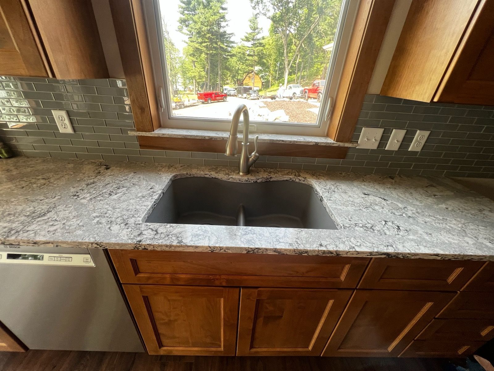 Kitchen with granite countertop, double sink, wood cabinets, window with view of trees.