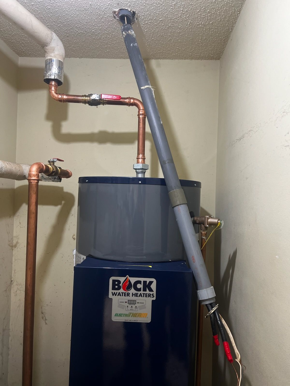 Water heater with copper pipes and a vertical flue pipe in a utility room.