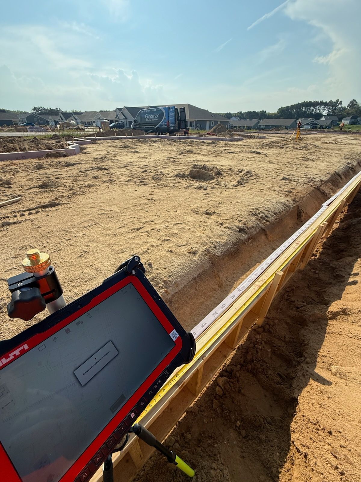 Construction site with a tablet, measuring tape, and survey equipment; sunny day.