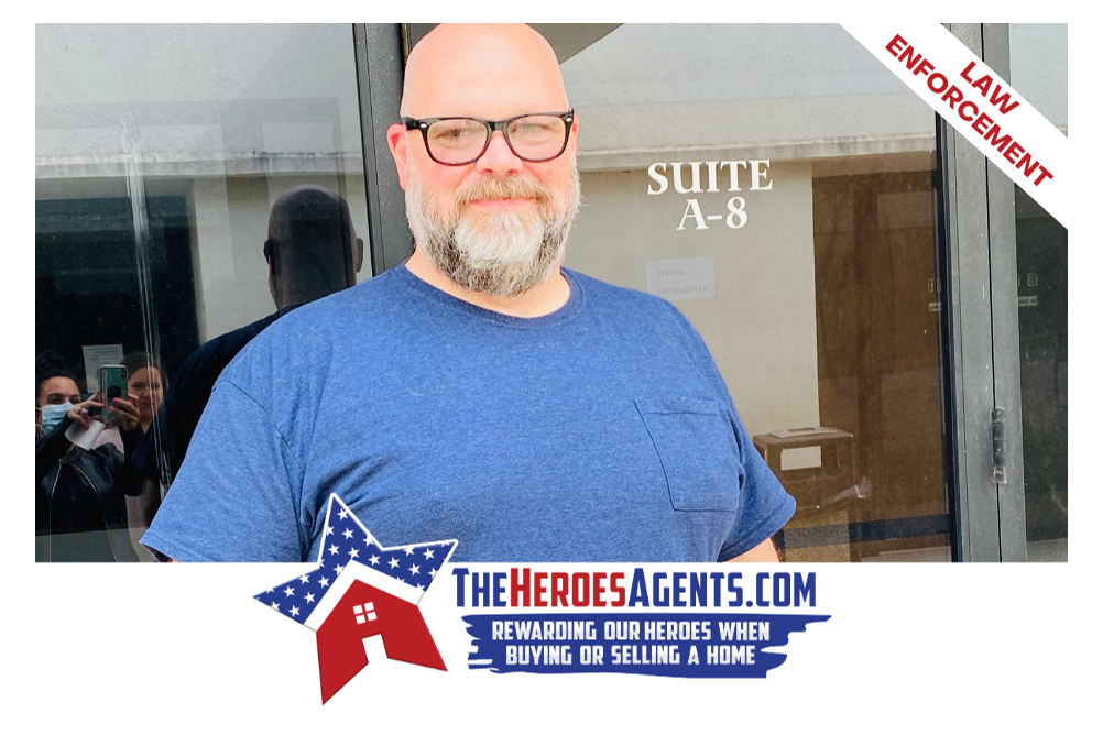 A bald man with glasses and a beard is standing in front of a building that says suite a-8.