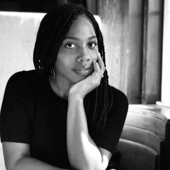 Woman with braided hair, rests chin on hand, looking towards the camera.