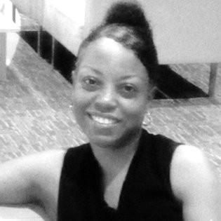 Woman with dark hair in a bun smiling, wearing a black sleeveless top, indoors.