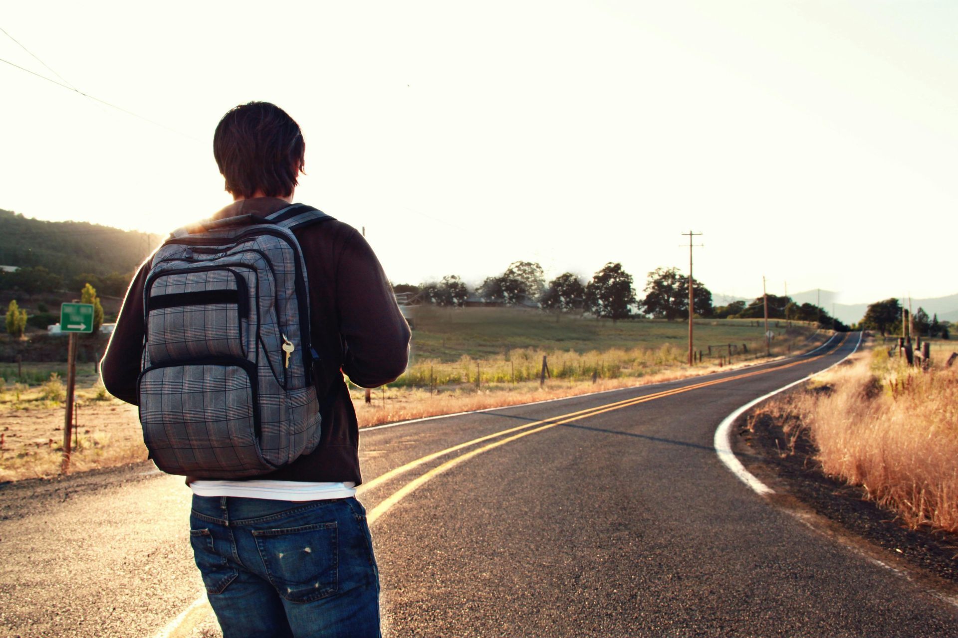 Person with backpack walks on a road, golden hour sunlight.
