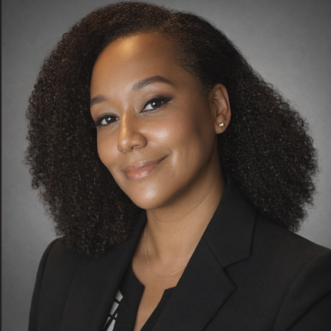 Woman smiling, leaning in, arm at cheek, wearing black jacket, dark curly hair.