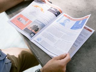 Person reading an open magazine with colorful pages at a table