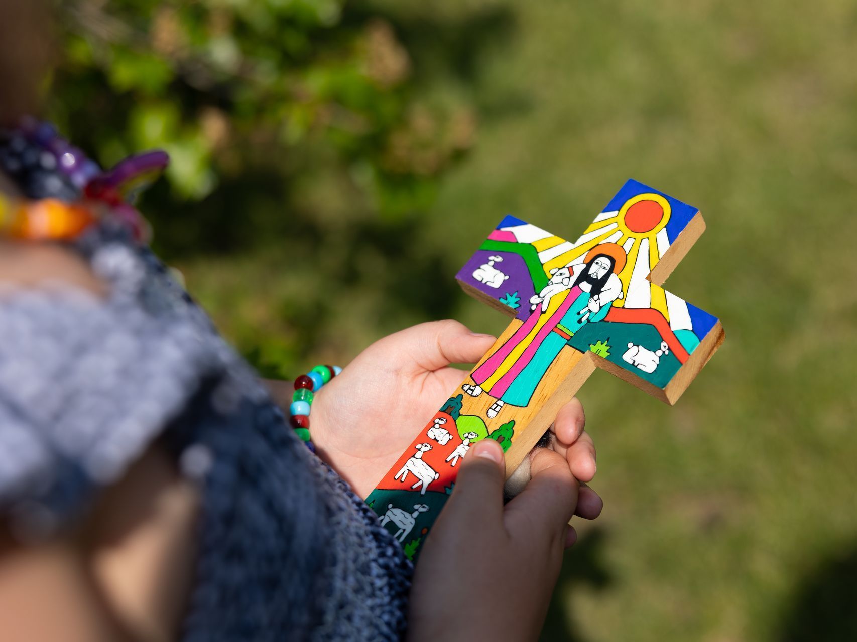 Hands holding a colorful cross-shaped craft against a blurred green background