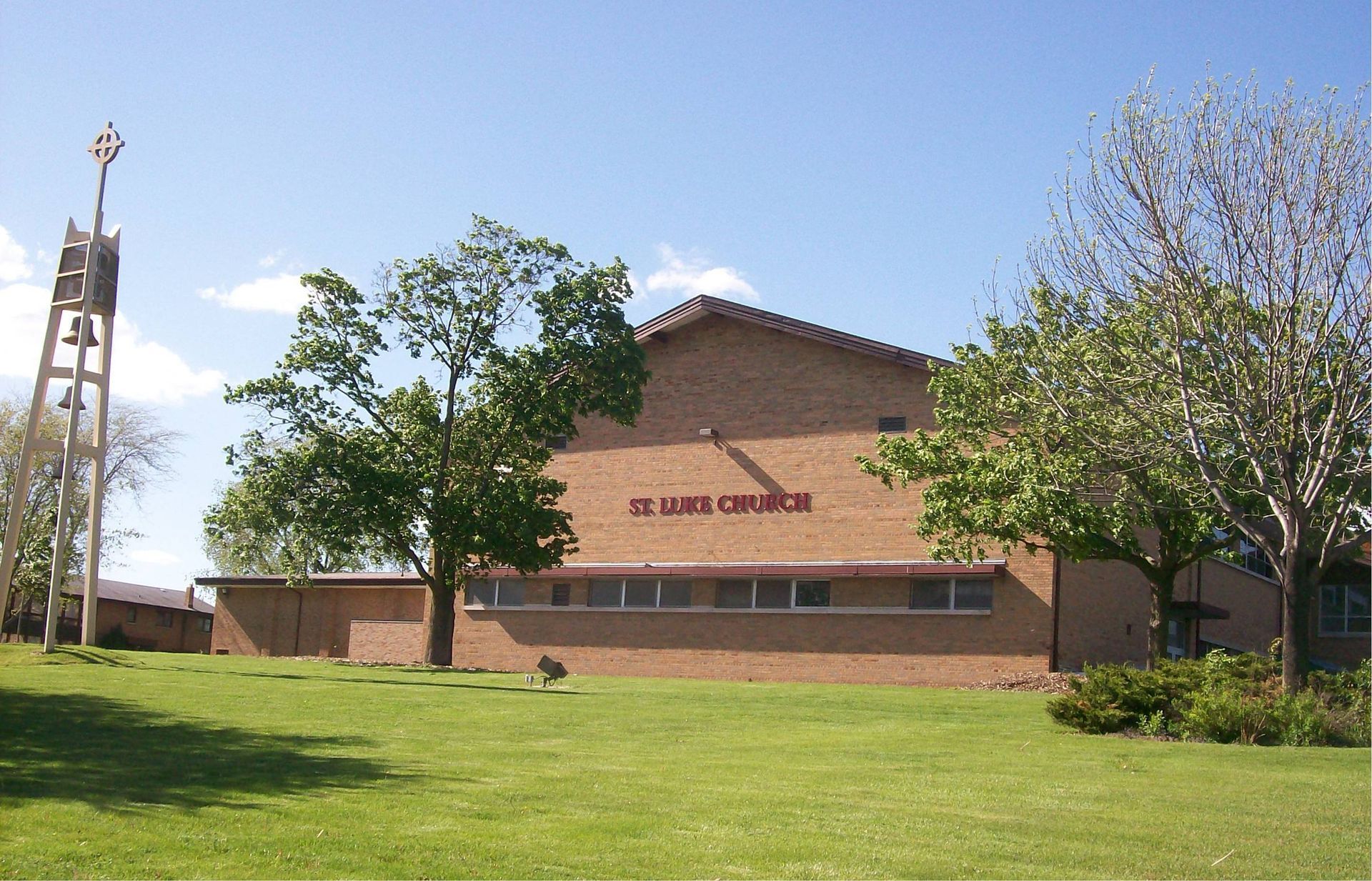 Brick church building with a cross tower, green lawn, and trees under a blue sky