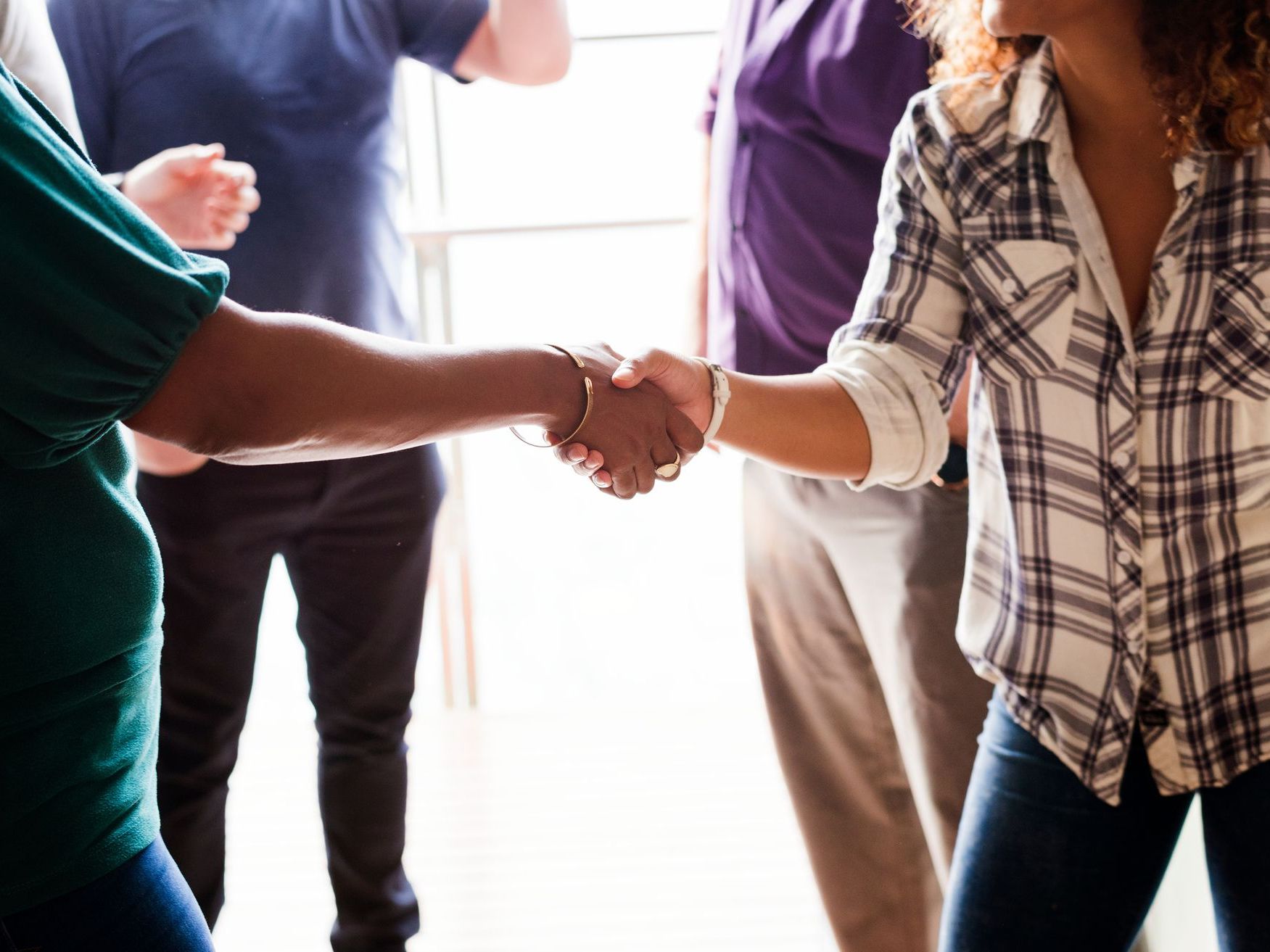 People shaking hands in a bright office hallway, with others standing nearby in casual clothes