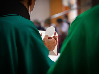 Person in green robe holding a white communion wafer during a church service