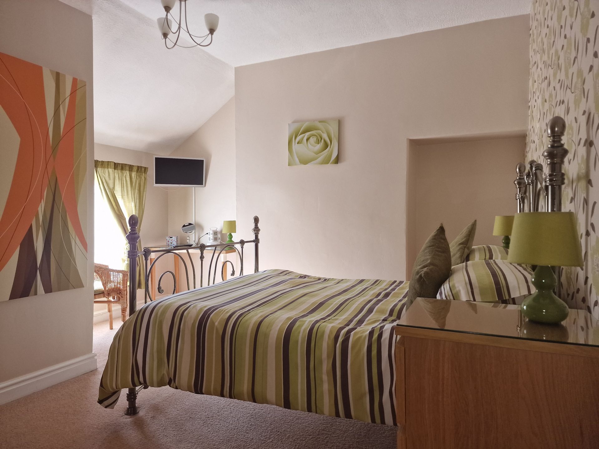 A bedroom with a bed , dresser , lamps and a television.