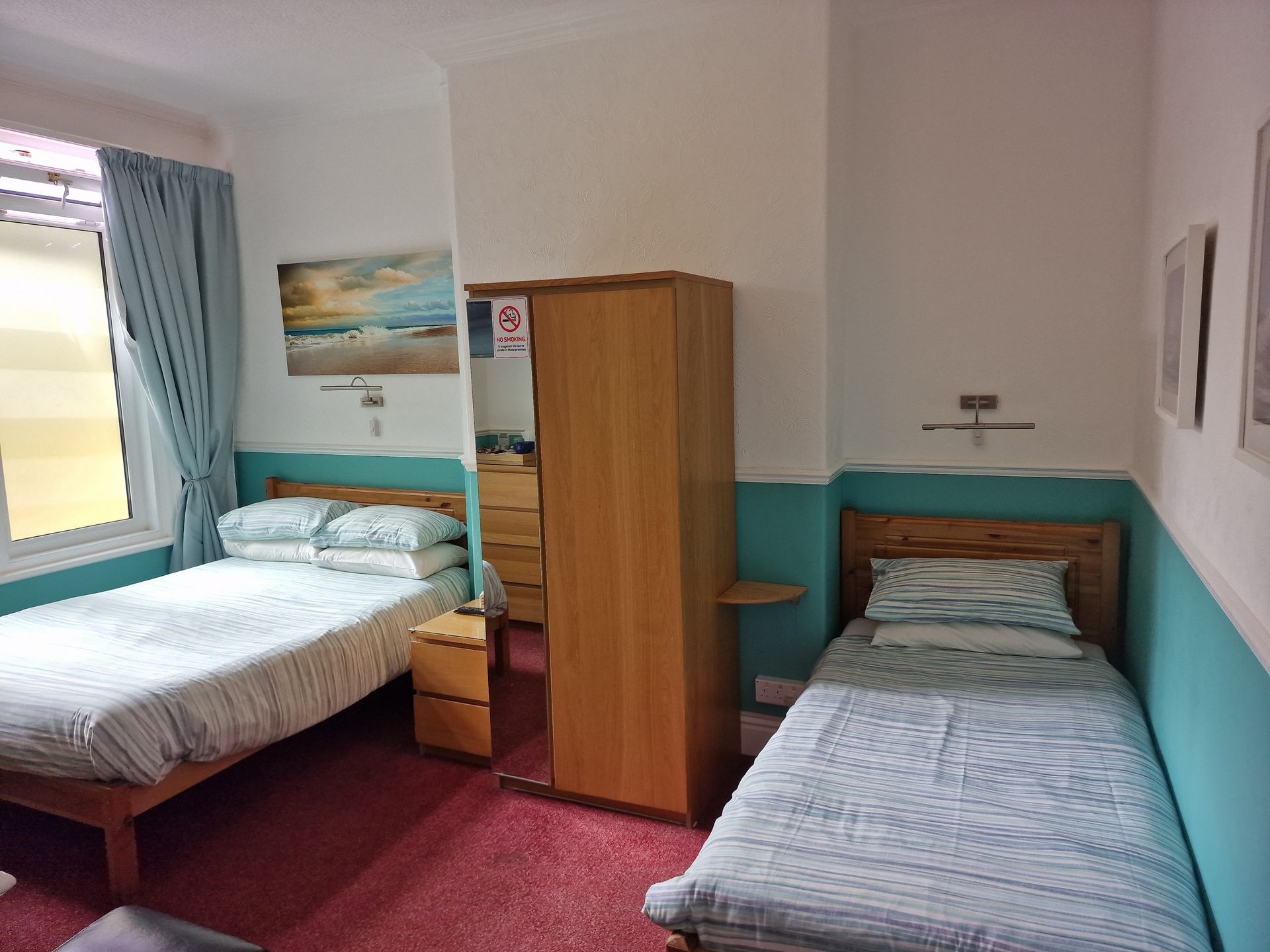 A bedroom with two beds , a wardrobe and a mirror.