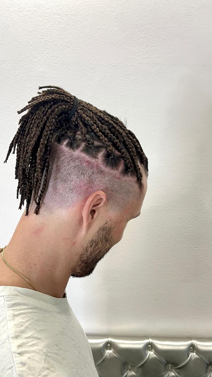 Un uomo con i dreadlock e la testa rasata indossa una camicia bianca.