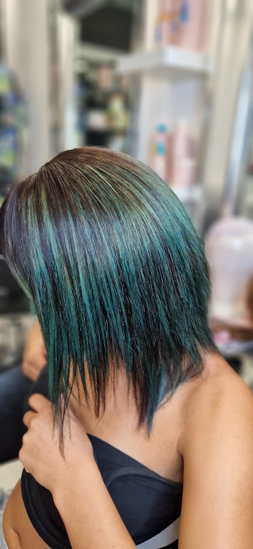 Una donna con i capelli verdi è seduta davanti allo specchio in un salone.