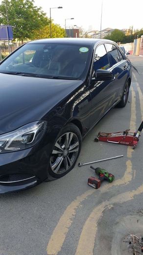 A black car is sitting on a jack in a parking lot.