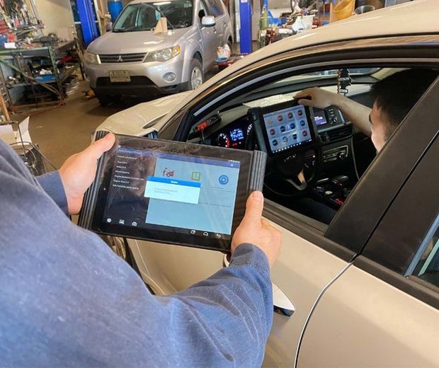 A man is holding a tablet in front of a car.