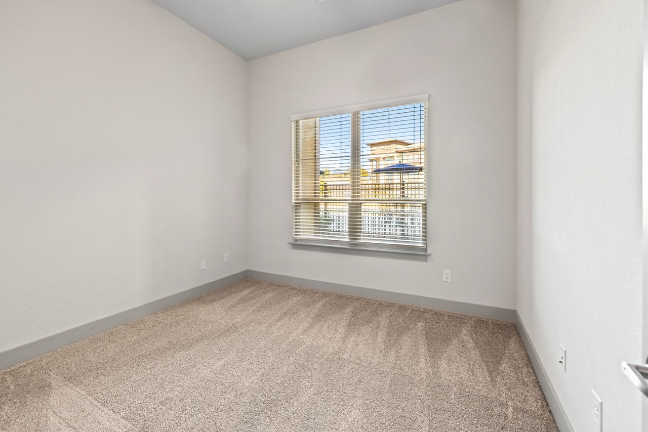 Empty, carpeted room with a window and horizontal blinds.