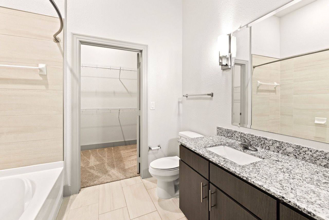 Bathroom with granite countertop, double-sink vanity, toilet, tub/shower, and walk-in closet.