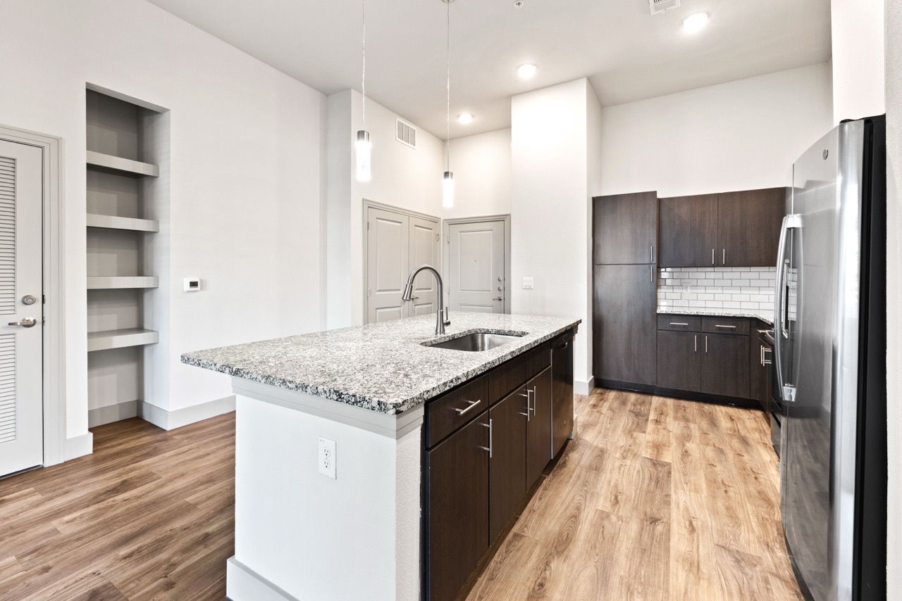 Modern apartment kitchen with granite island, dark wood cabinets, and stainless steel appliances.