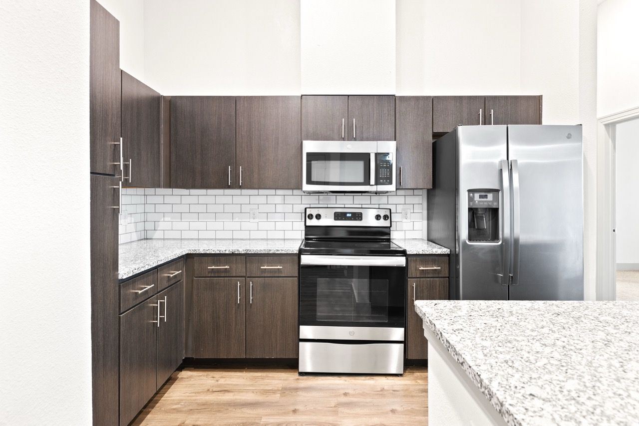 Modern apartment kitchen with dark wood cabinets, stainless steel appliances, and granite countertops.