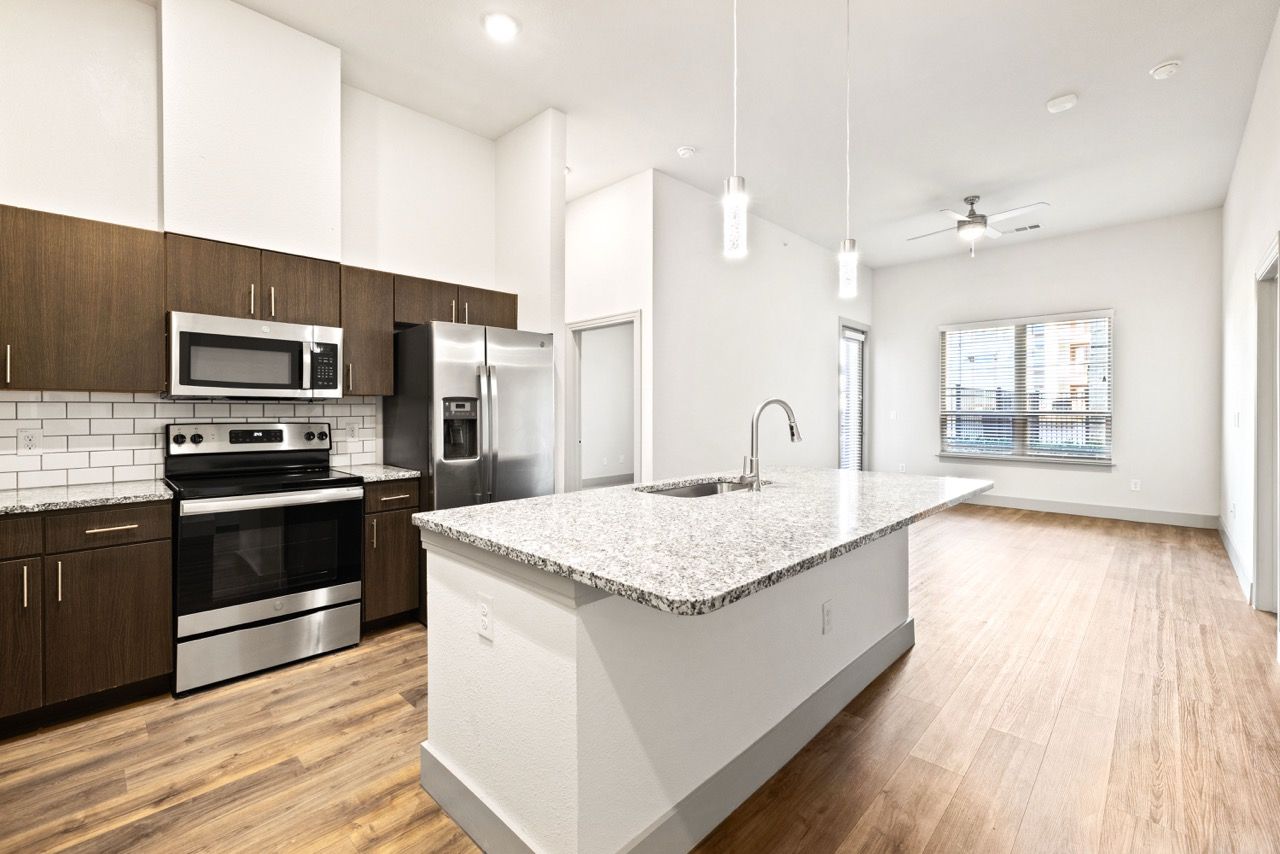 Modern kitchen with granite island and stainless steel appliances in an open living area.