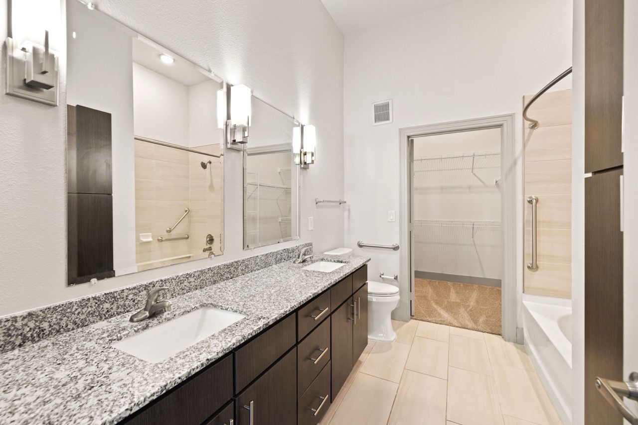 Apartment bathroom with granite double vanity, mirrors, and tub/shower.