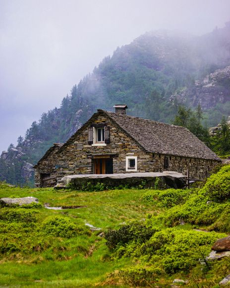 A stone house in the middle of a grassy field in the mountains.