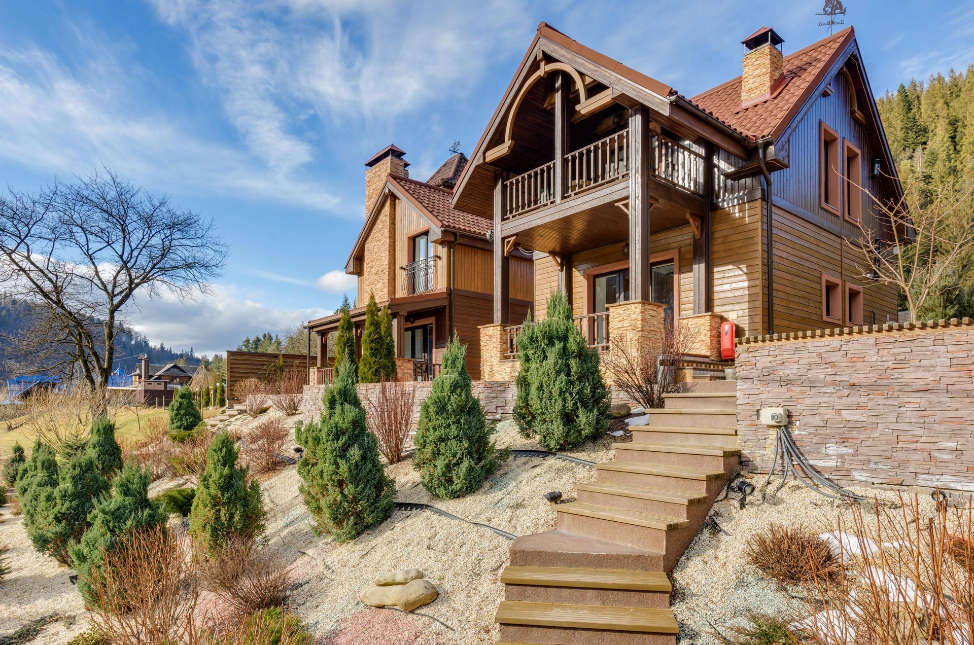A large house with stairs leading up to it is surrounded by trees and bushes.