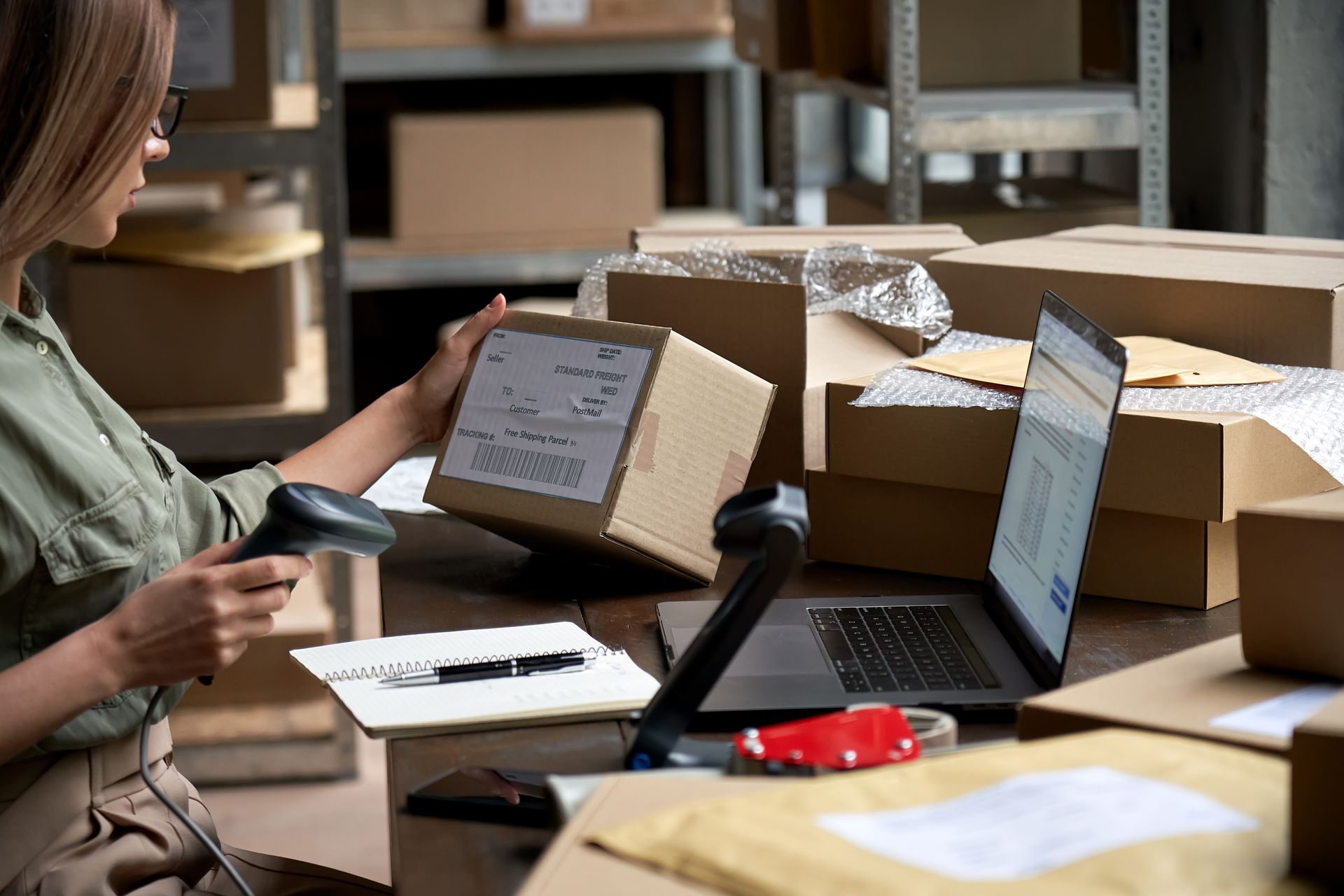 A woman is using a scanner to scan a box in a warehouse.