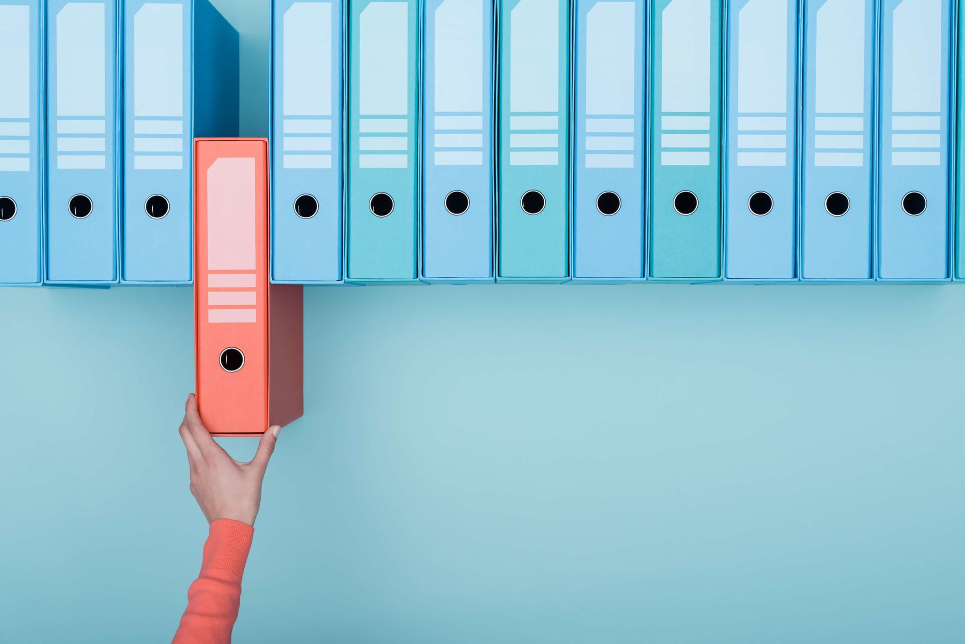 A person is holding a red binder in front of a row of blue binders.