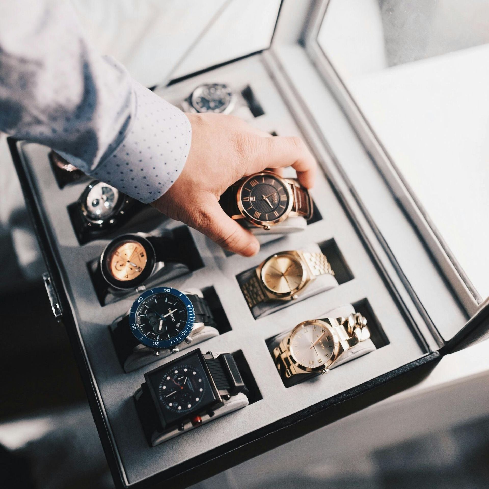 A person is holding a watch in a case of watches