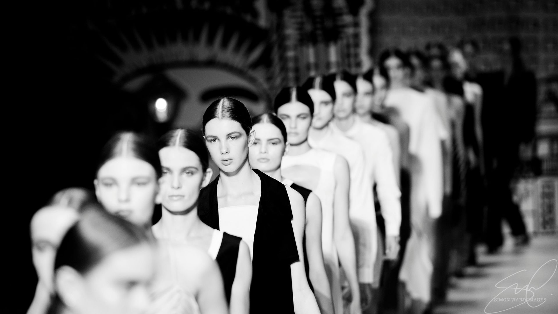 A black and white photo of a row of women walking down a runway.