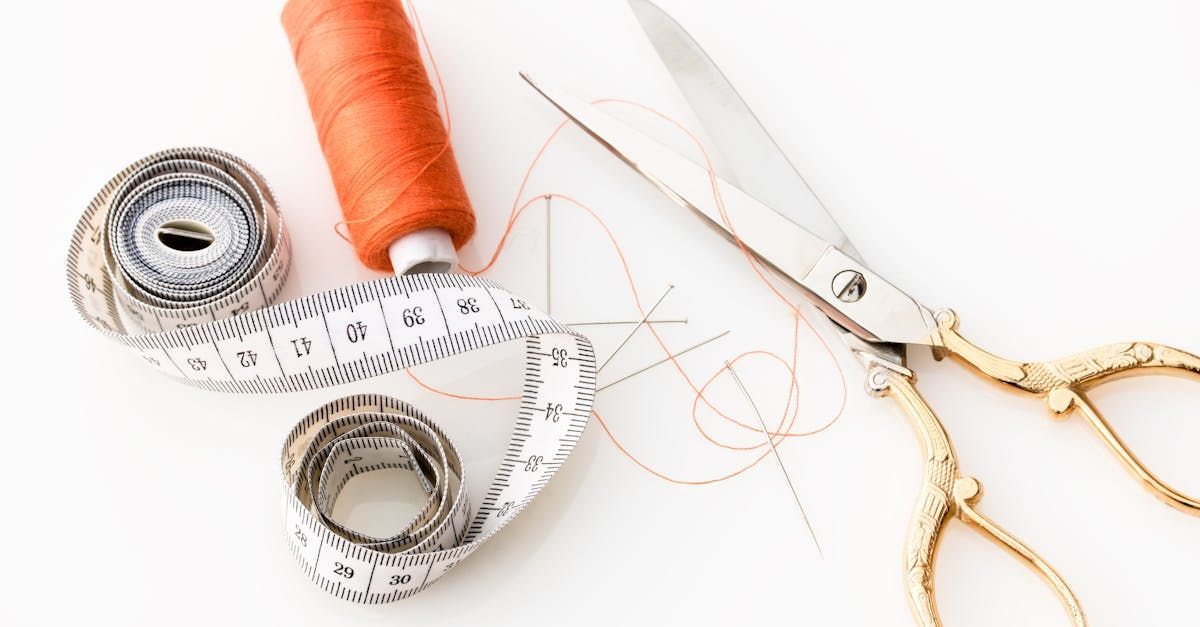 A pair of scissors , a spool of thread , and a measuring tape are on a table.