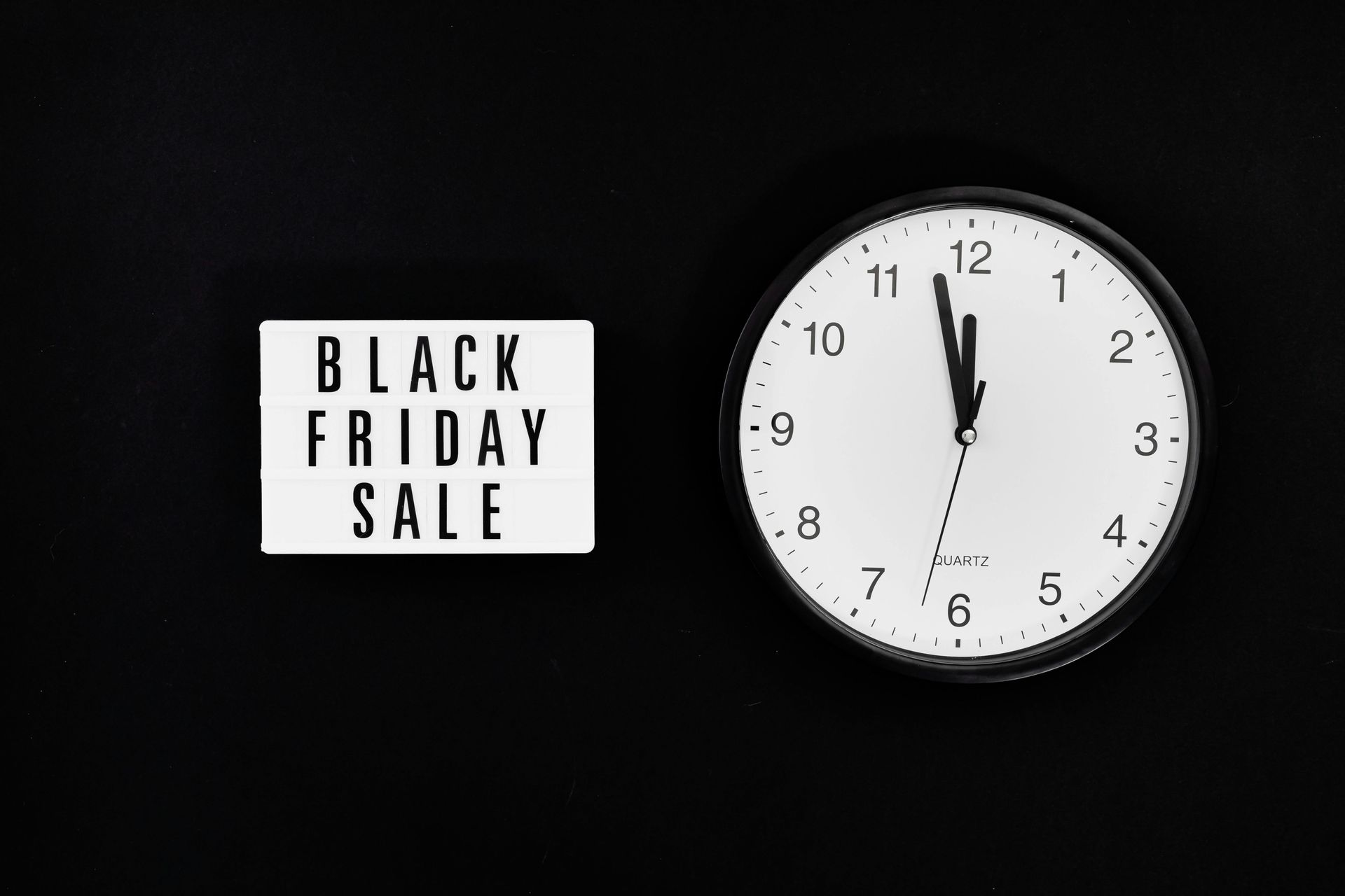 A black friday sale sign next to a clock on a black background.